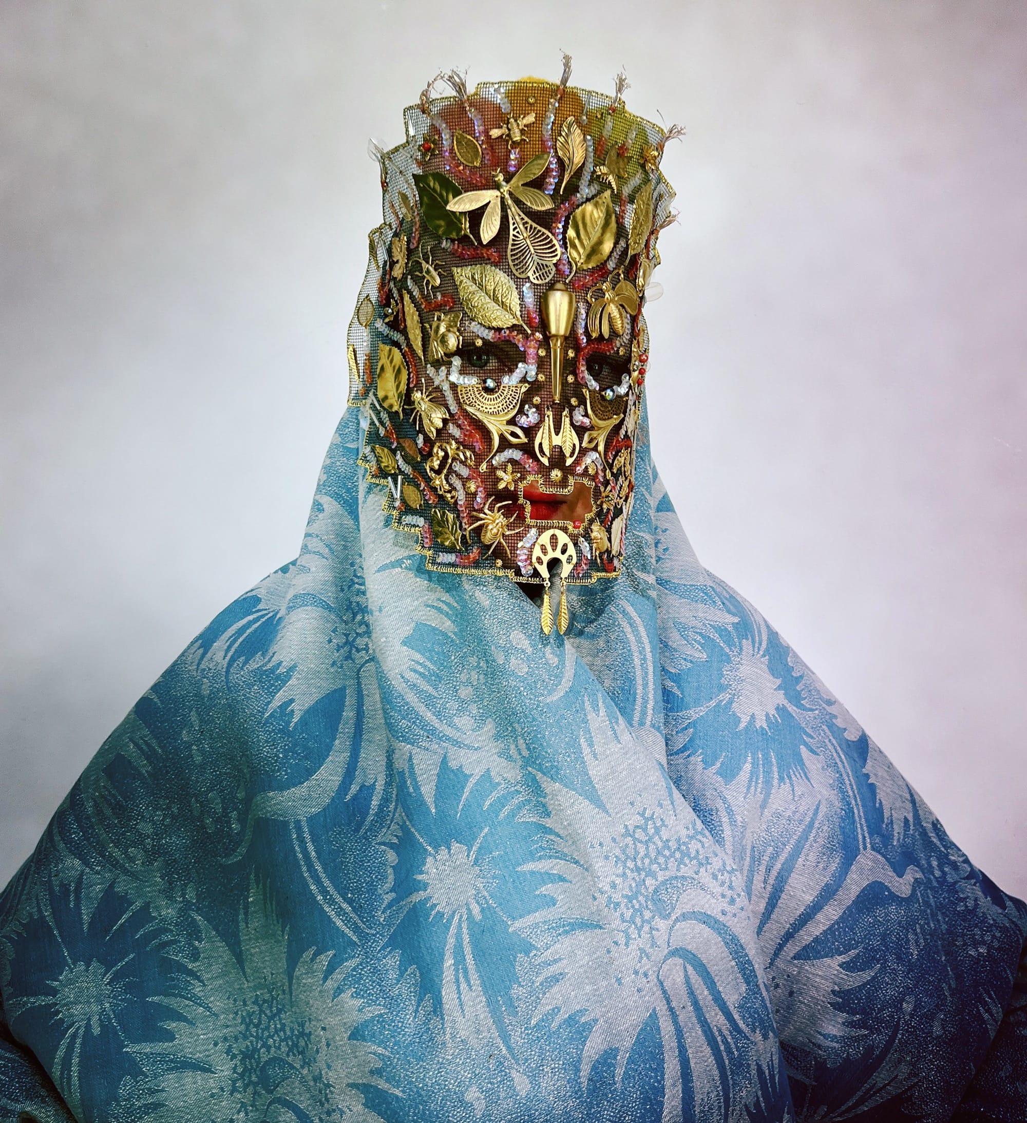 an ornate mask by Magnhild Kennedy with gold and red details, and a patterned blue textile covering the body
