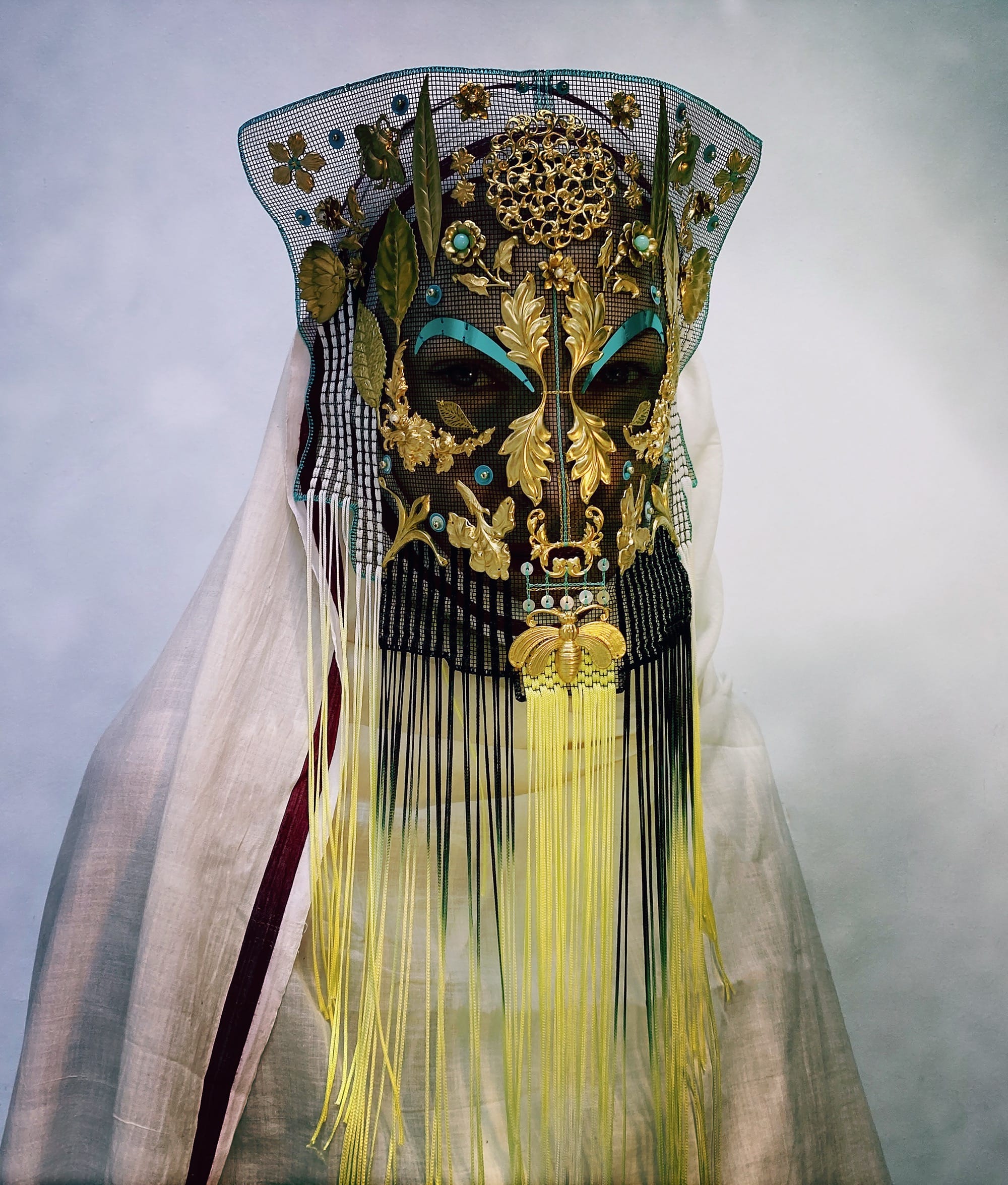 an ornate mask by Magnhild Kennedy with yellow and black beads and fringe and a textile covering the body