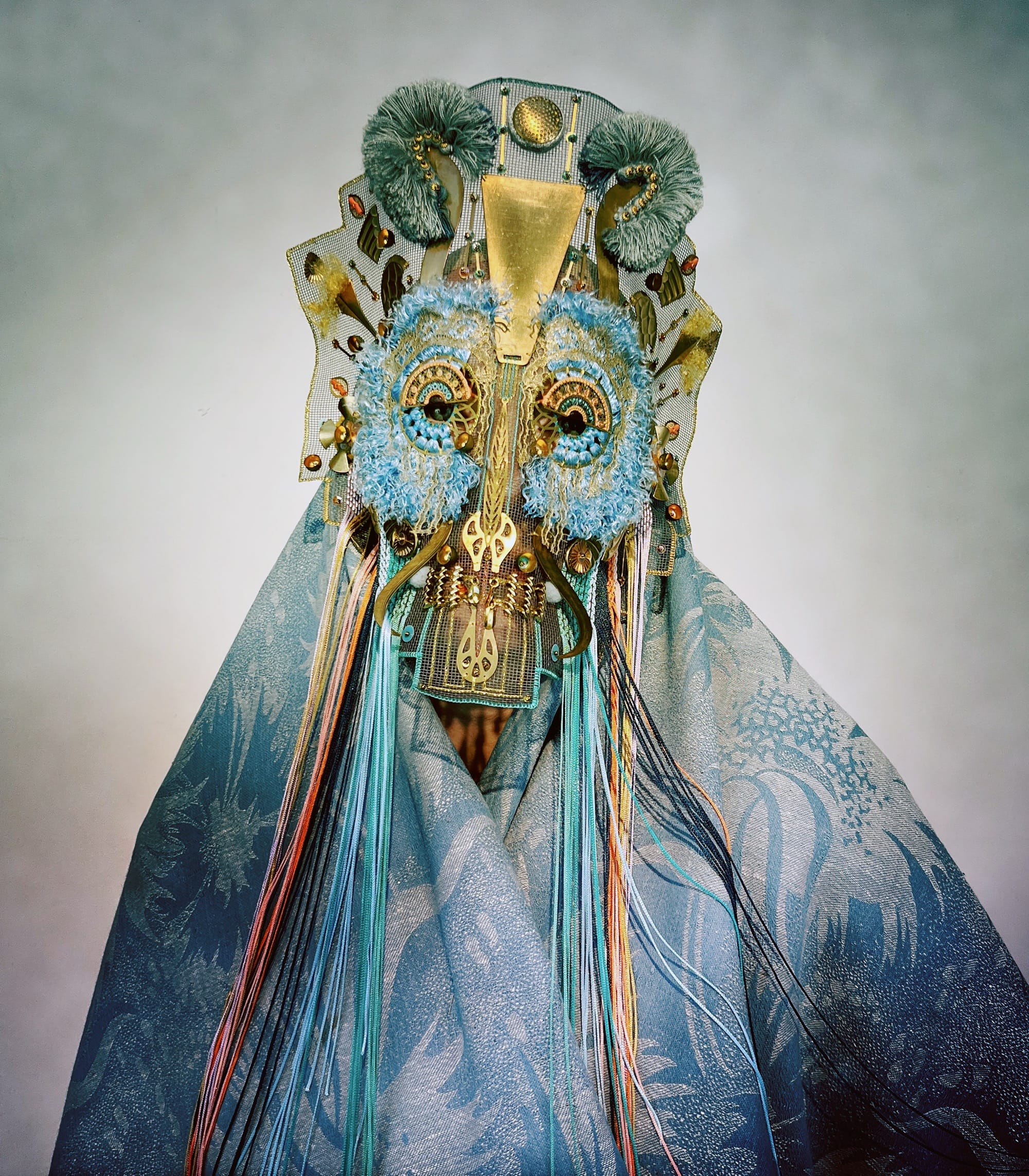 an ornate mask by Magnhild Kennedy with yellow and blue beads and details and a patterned blue textile covering the body